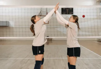 Image of two teen ladies high fiving near a volleyball net