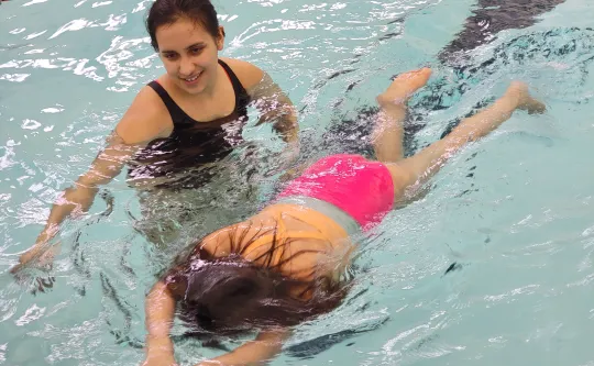 Woman in pool with a young girl teaching her to swim with her face in the water