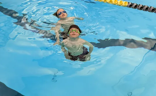 Two children in the deep end of a pool floating