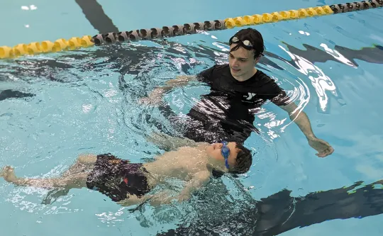 An adult swim instructor teaching a child wearing goggles to float on their back