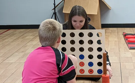 A photo of two young people playing a giant connect four game