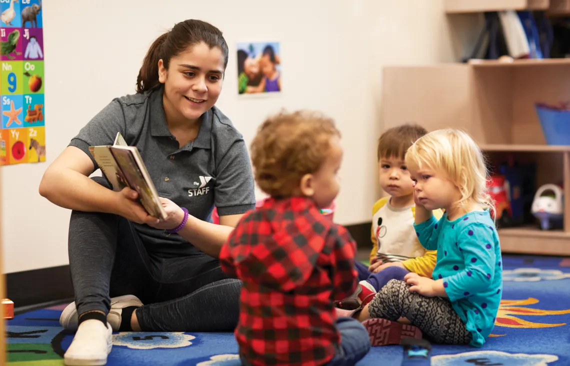 An adult woman reading a book with pre-school children.