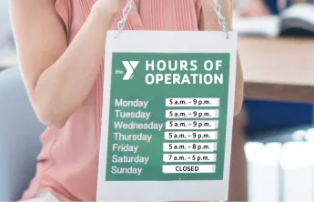 Woman holding up a sign with  hours of operation for YMCA branch hours