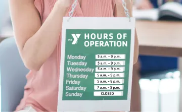 Woman holding up a sign with  hours of operation for YMCA branch hours